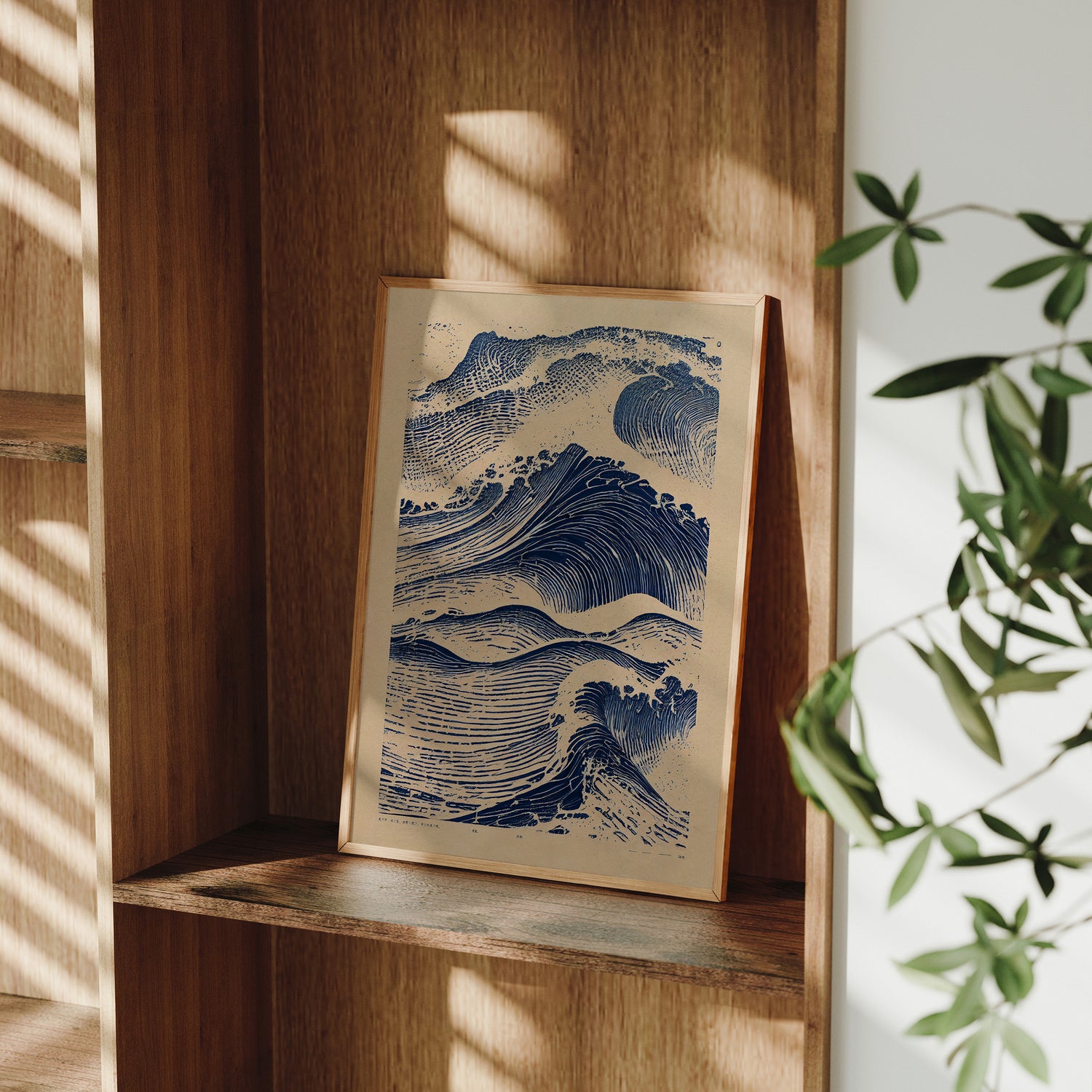 Framed artwork of a wave on a wooden shelf with natural light and plant in the background